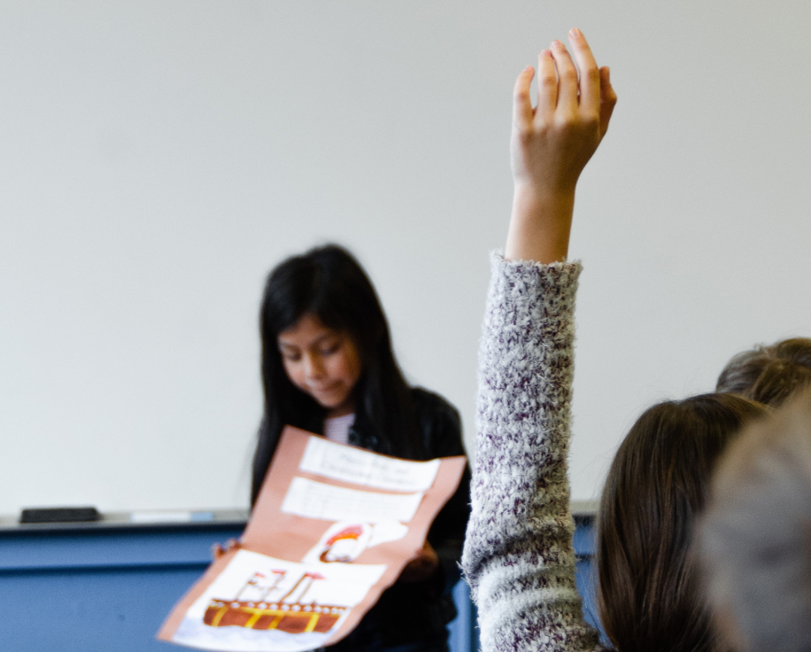 elementary school student presenting with another student raising their hand