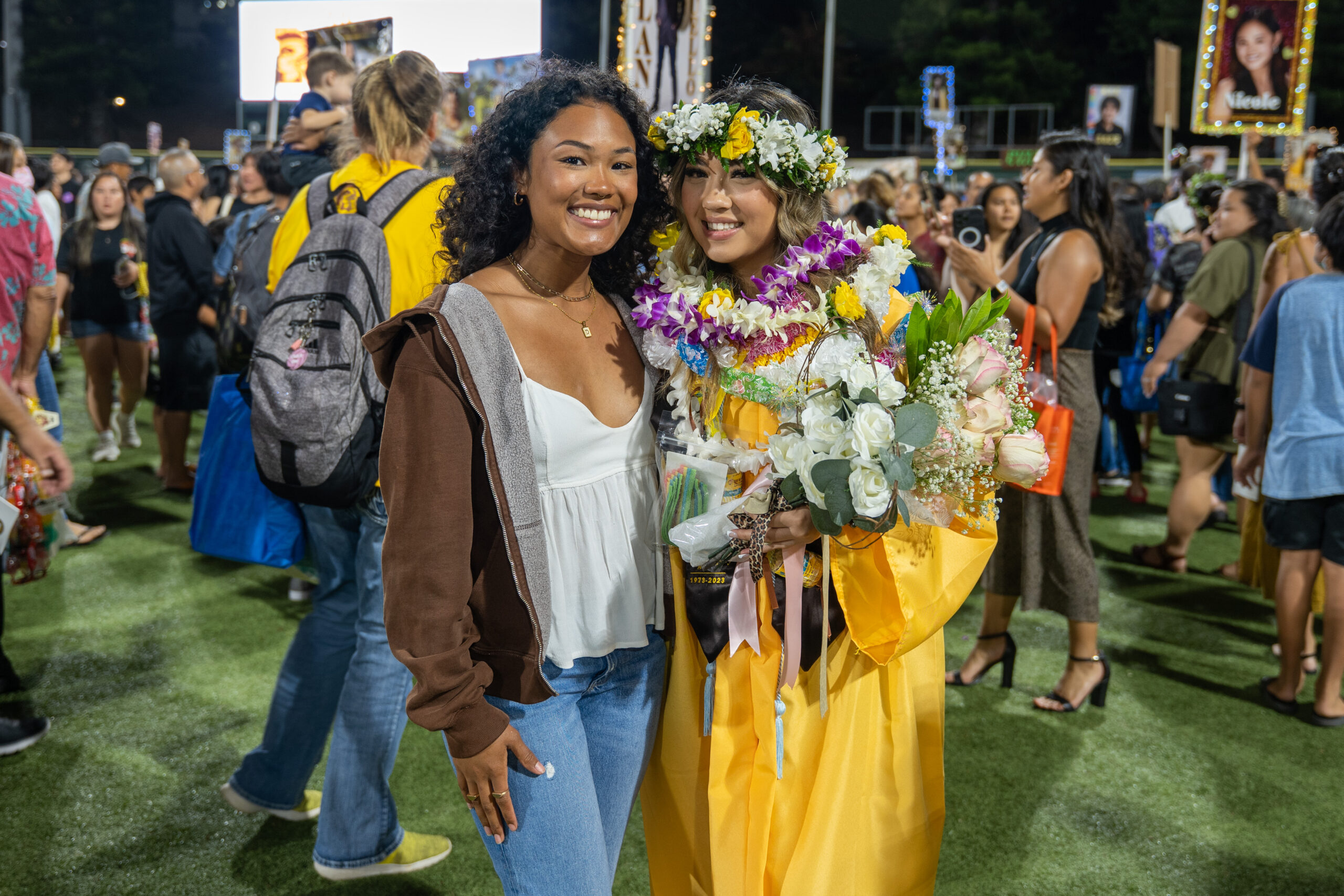 High school graduate with lei posing for picture with a friend