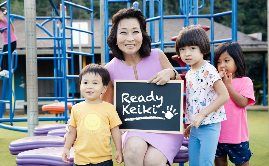 Lieutenant Governor Sylvia Luke holding a Ready Keiki sign with three young children on a jungle gym